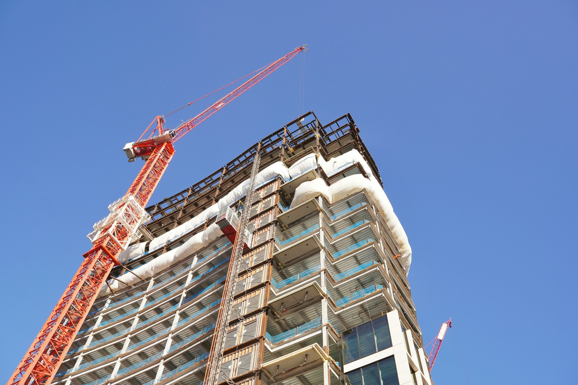High-rise building under construction with a red tower crane against a clear blue sky