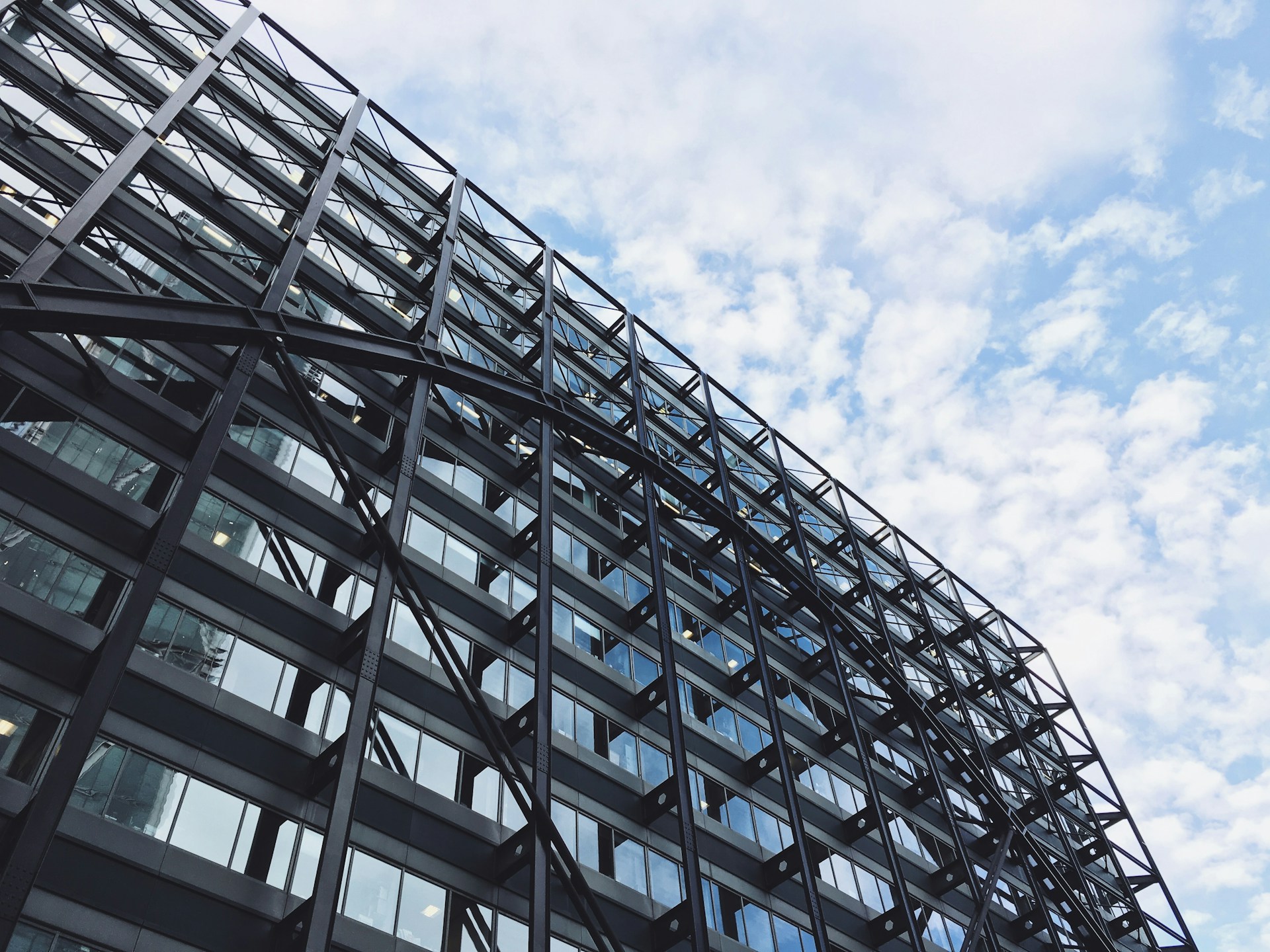 Glass and steel office building viewed from below against a partly cloudy sky