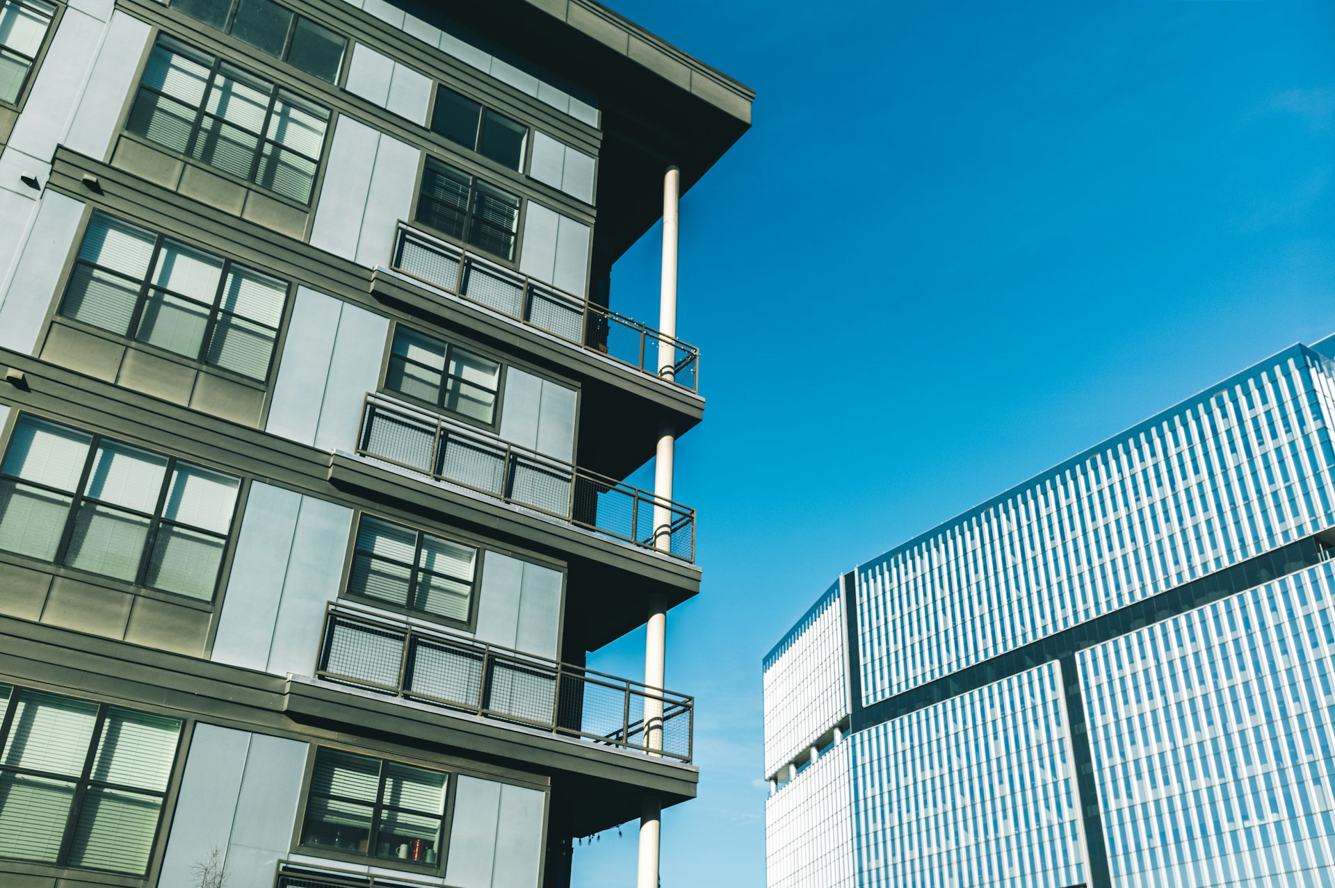 Modern apartment building with balconies next to a glass office block under a blue sky